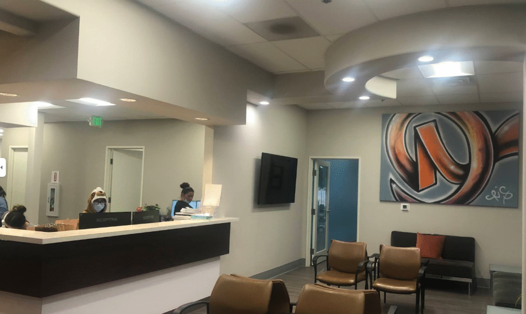 Rockville Smiles waiting area with empty chairs, a reception desk with staff, wall art, and overhead lighting welcomes patients to Rockville Smiles Dentistry for top pediatric dental care.